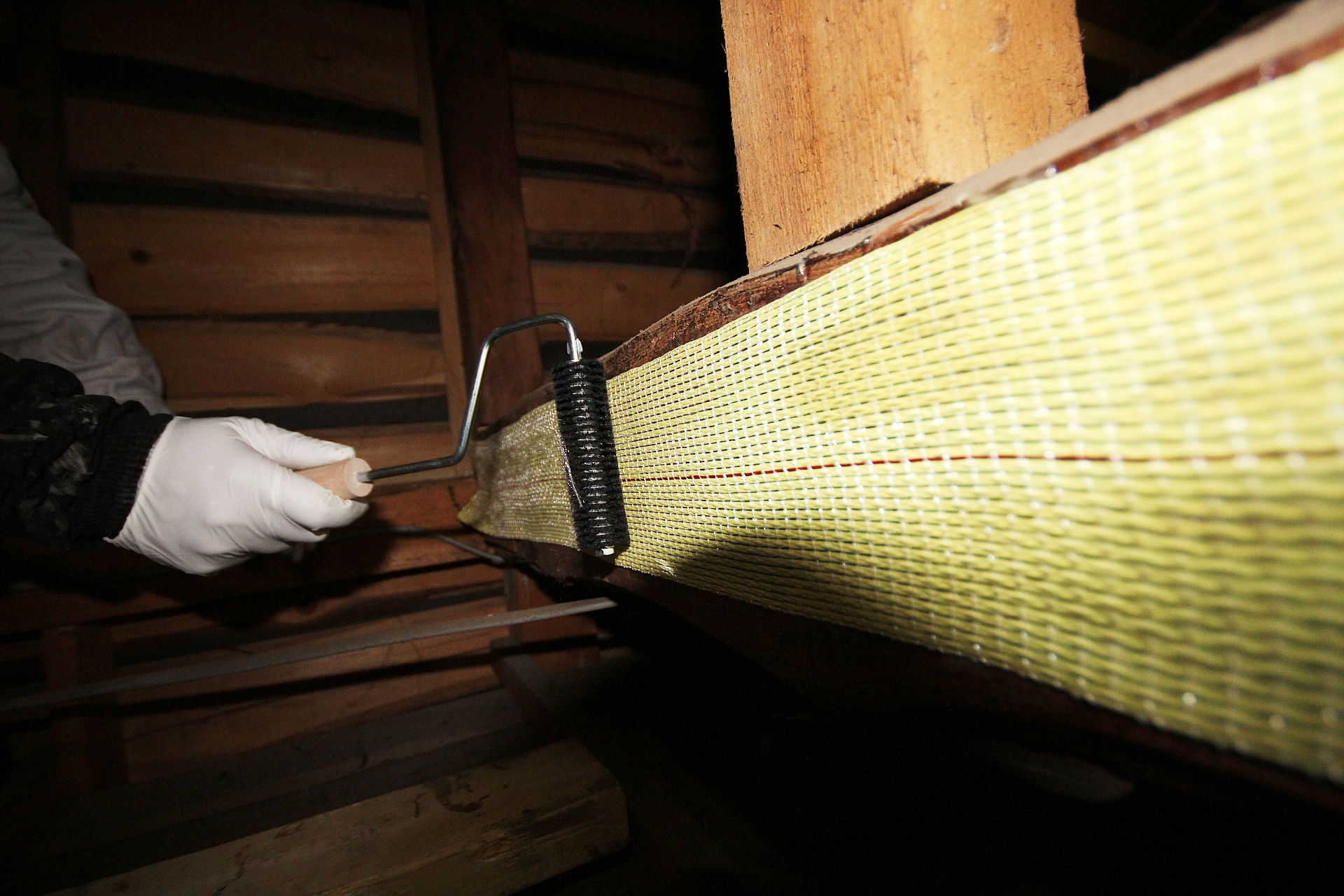 木材に貼ったアラミド繊維シートをローラーで圧着する木部補強の施工