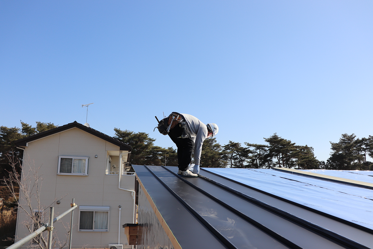住宅屋根の上で作業箇所を確認する職人